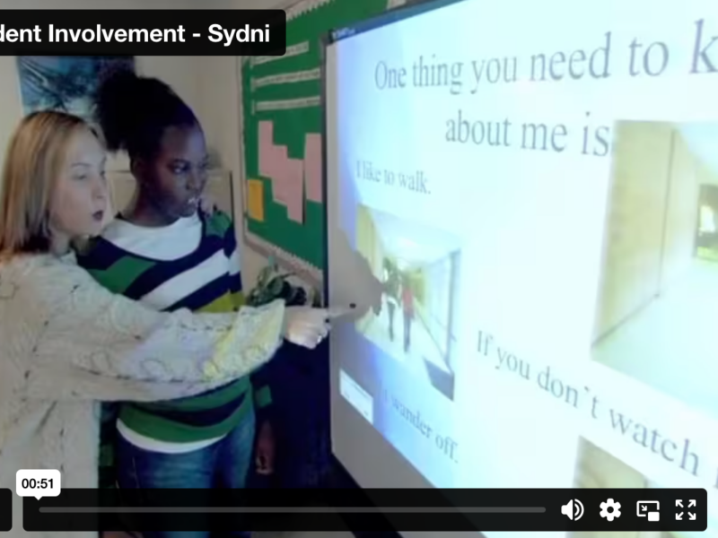 Sydni IEP Participation Screenshot of video showing Sydni and her teacher at a SmartBoard, pointing to her IEP presentation.