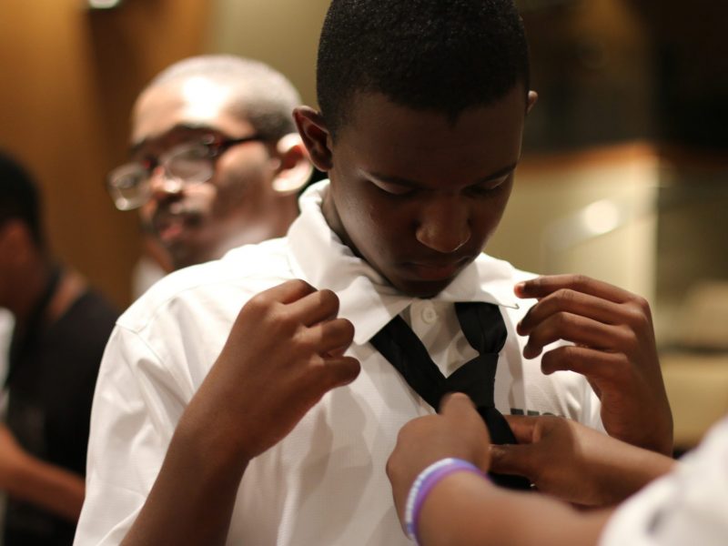 a young man receives help in tying a formal tie around a collared shirt