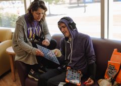 a teacher helps a teenage boy communicate with a letter-board