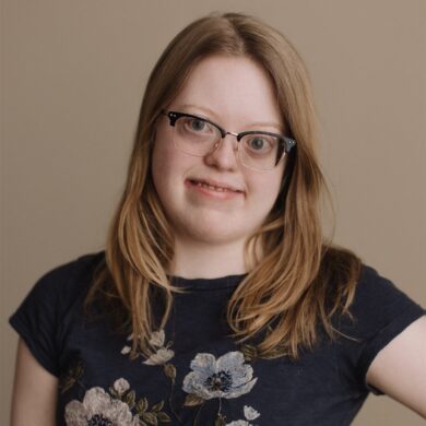 Sydney smiling, wearing a shirt with floral print, hand on hip