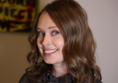 Headshot of Erin Saxon, female with shoulder-length brown hair, smiling, wearing a black shirt with small white dots