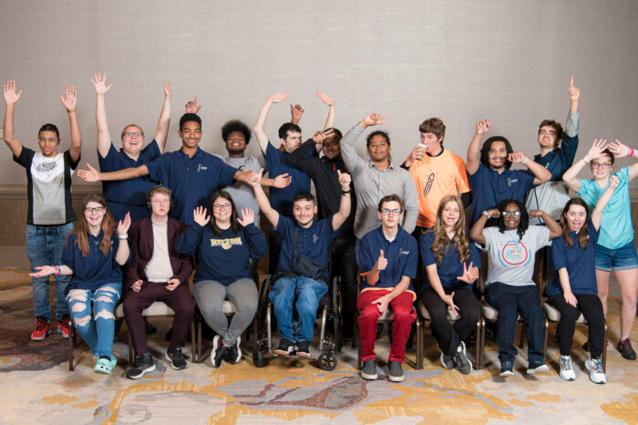 Group photo of the I'm Determined State Youth Leaders in two rows, one seated and one standing behind the first row. Everyone is wearing colorful clothing, smiling and raising their hands, waving to the camera, or giving a thumbs up.