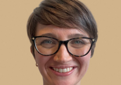 Headshot of BethAnne, smiling and wearing glasses and a black shirt with small flowers.