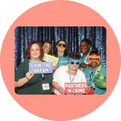 Six employees from the Virginia Department of Education posing for the photo booth at the Youth & Family Summit. They are all holding or wearing funny props and have signs that say, "Vibing," "Livin' the dream," and "Partners in crime."