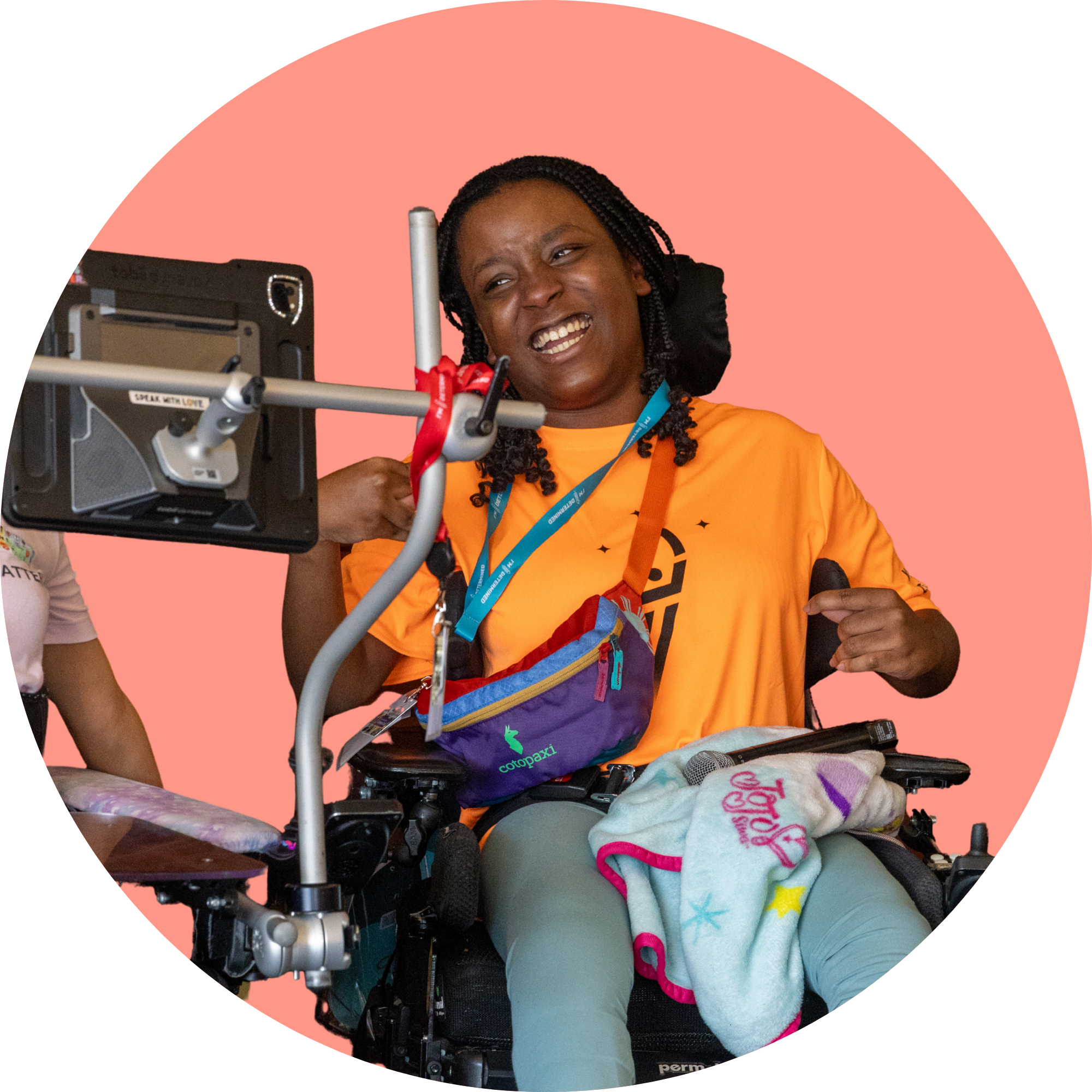Youth Leader Natia smiling and with a microphone in her lap. On the left side of the photo is another Youth Leader's communication device mounted to her wheelchair.