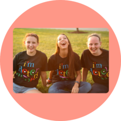 Three I'm Determined Youth Leaders sit on the grass, smiling, wearing a black t-shirt with the I'm Determined logo on the front.