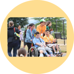 Two I'm Determined Youth Leaders using wheelchairs get pushed by other I'm Determined team members during outdoor activities at the Youth & Family Summit.